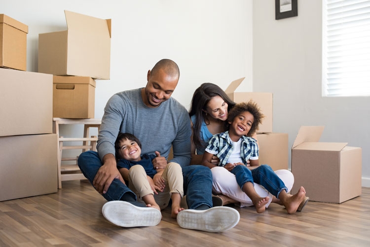 A family of four sitting on the floor of their new home with cardboard boxes around them