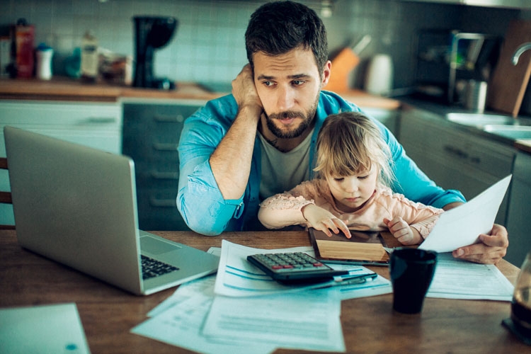 A man with his son sitting on his lap. He is looking at a laptop with a concerned look on his face. A man with his son sitting on his lap. He is looking at a laptop with a concerned look on his face.